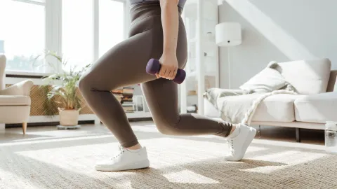 Mulher fazendo lunge com halteres na sala de casa