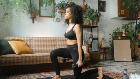Mulher treinando com halteres na sala de casa