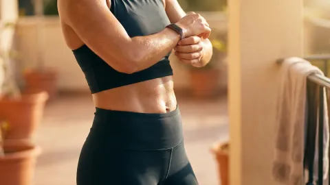 Mulher ajustando o smartwatch após treino intenso na varanda de casa
