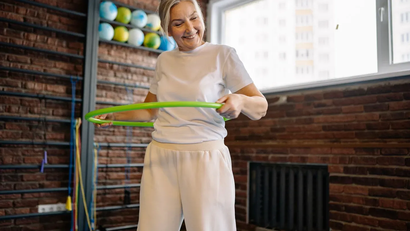 Mulher idosa sorrindo enquanto se exercita em ambiente iluminado Mulher idosa sorrindo enquanto se exercita em ambiente iluminado