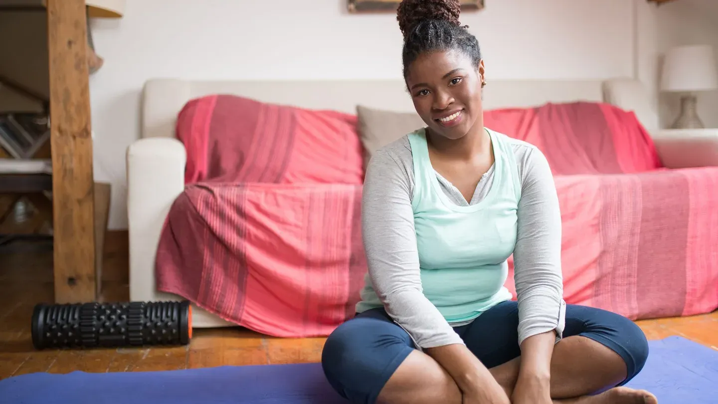 Mulher sorrindo sentada em tapete de exercícios pronta para treinar