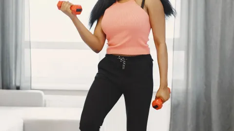 Mulher sorrindo treinando com halteres em casa