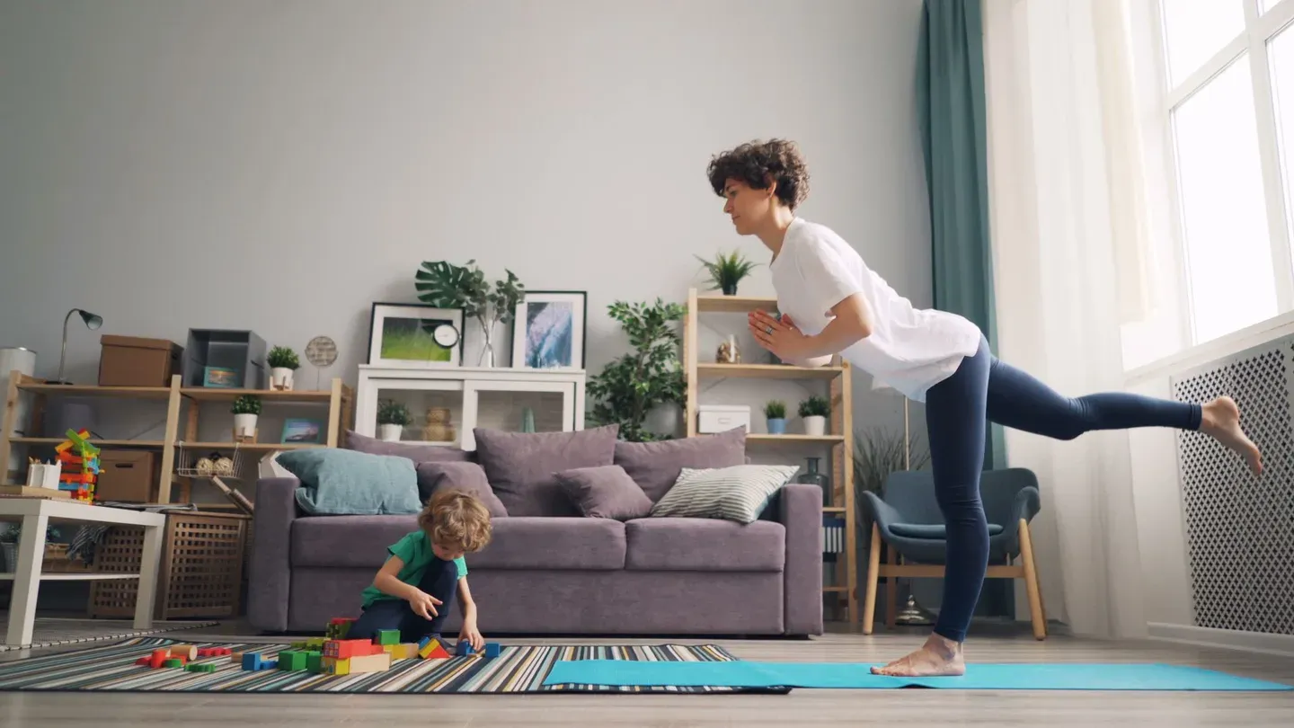 Mãe se exercitando na sala enquanto o filho brinca no tapete ao lado