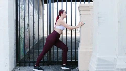 Mulher alongando a panturrilha empurrando parede, joelho de trás estendido