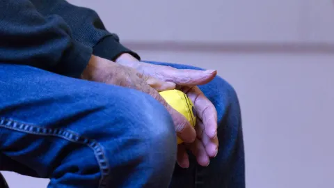 Mão de pessoa idosa segurando bola para teste de força de preensão