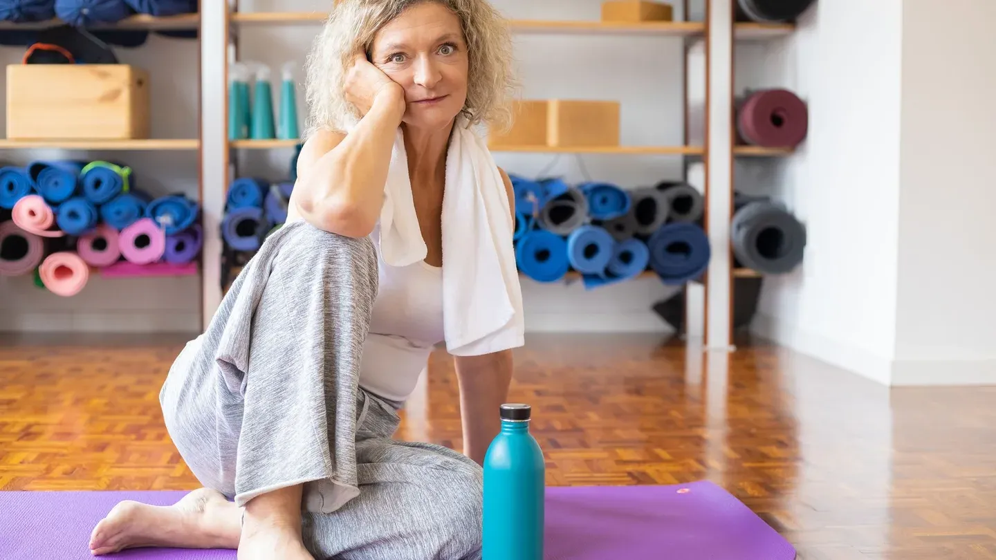 Mulher descansando sentada no tapete de exercícios com garrafa de água Mulher descansando sentada no tapete de exercícios com garrafa de água