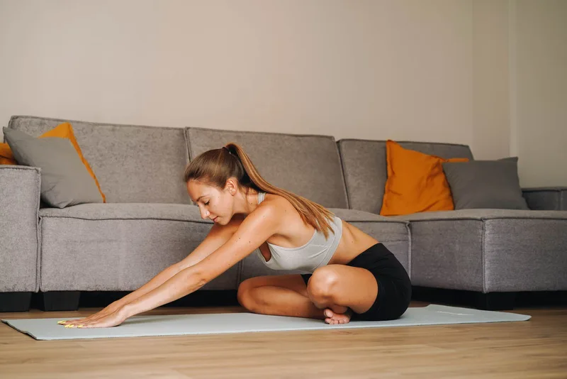 Mulher sentada no chão da sala alongando a lombar e os isquiotibiais, tronco inclinado para frente Mulher sentada no chão da sala alongando a lombar e os isquiotibiais, tronco inclinado para frente