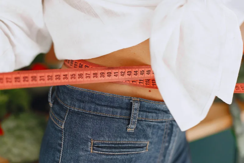 Close-up de fita métrica laranja medindo a cintura por cima da calça jeans