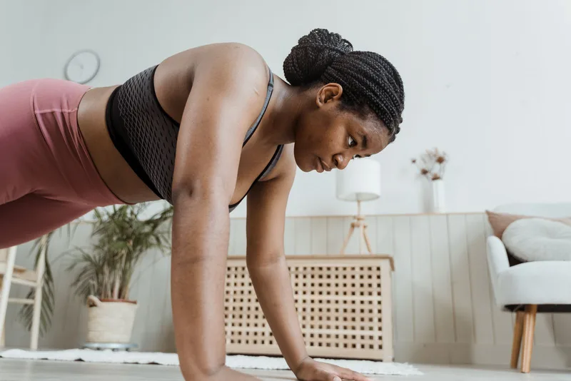 Mulher na posição de prancha alta na sala de casa, braços estendidos e corpo alinhado, ponto de partida do mountain climber