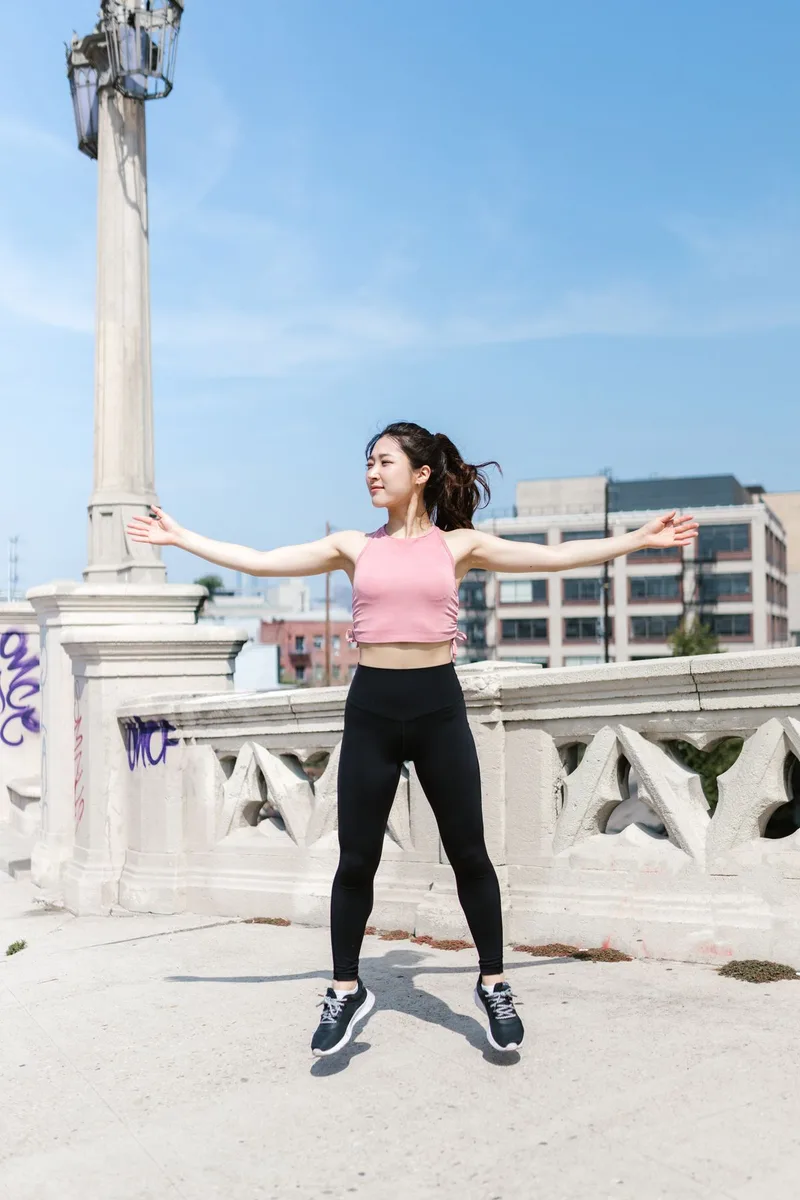 Mulher em movimento de salto com os braços abertos, exercício de HIIT e cardio