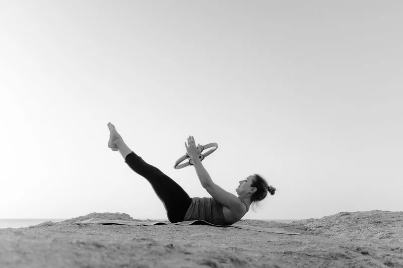 Mulher deitada segurando o anel de pilates acima do peito, com as pernas estendidas para cima, ativando o core Mulher deitada segurando o anel de pilates acima do peito, com as pernas estendidas para cima, ativando o core