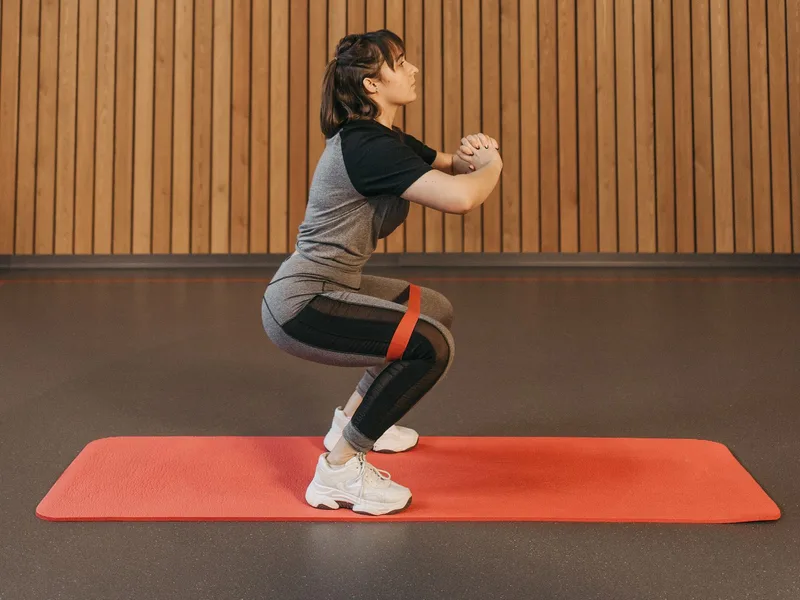 Mulher agachando com mini band acima dos joelhos sobre tapete de exercícios Mulher agachando com mini band acima dos joelhos sobre tapete de exercícios
