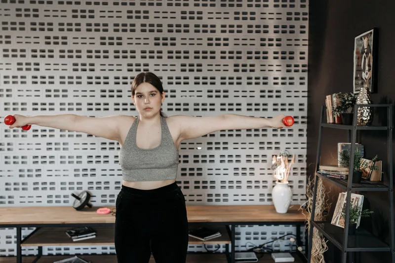 Mulher com os braços elevados lateralmente até a altura dos ombros, mesma amplitude usada na elevação lateral com elástico