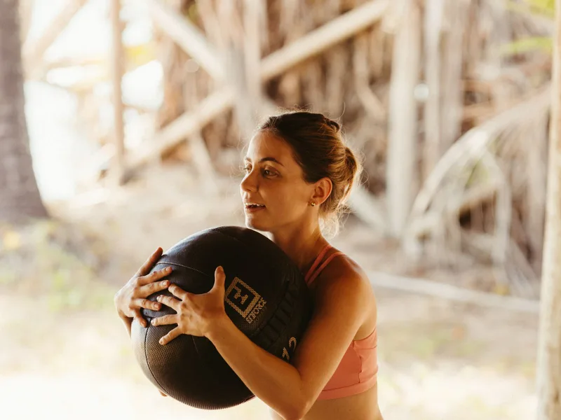 Mulher agachando segurando bola medicinal contra o peito, treino funcional
