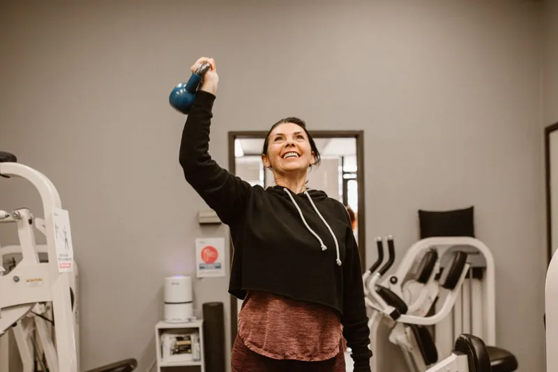 Mulher sorrindo enquanto levanta um kettlebell durante treino de força
