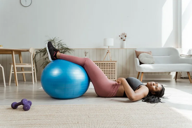 Mulher deitada com as pernas apoiadas em bola de pilates na sala de casa Mulher deitada com as pernas apoiadas em bola de pilates na sala de casa