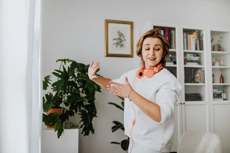 Mulher dançando na sala de casa com fones de ouvido no pescoço, sorrindo