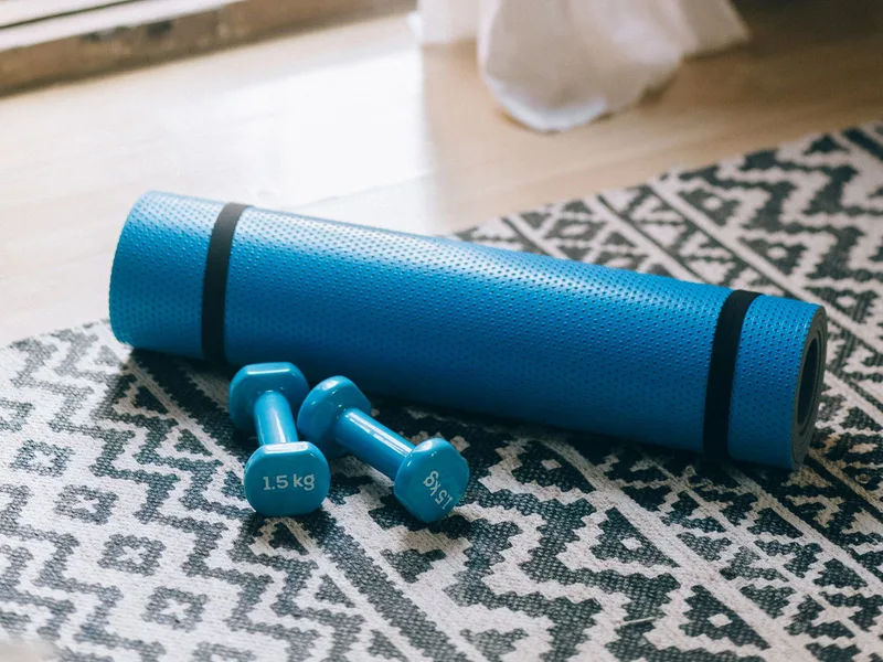 Colchonete azul e halteres de 1,5kg deixados à vista no chão da sala Colchonete azul e halteres de 1,5kg deixados à vista no chão da sala