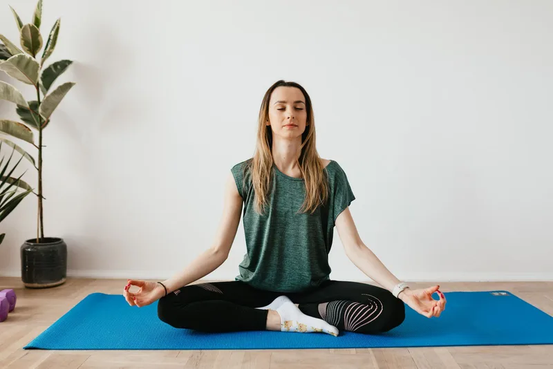 Mulher sentada em pose de meditação sobre tapete azul em casa Mulher sentada em pose de meditação sobre tapete azul em casa
