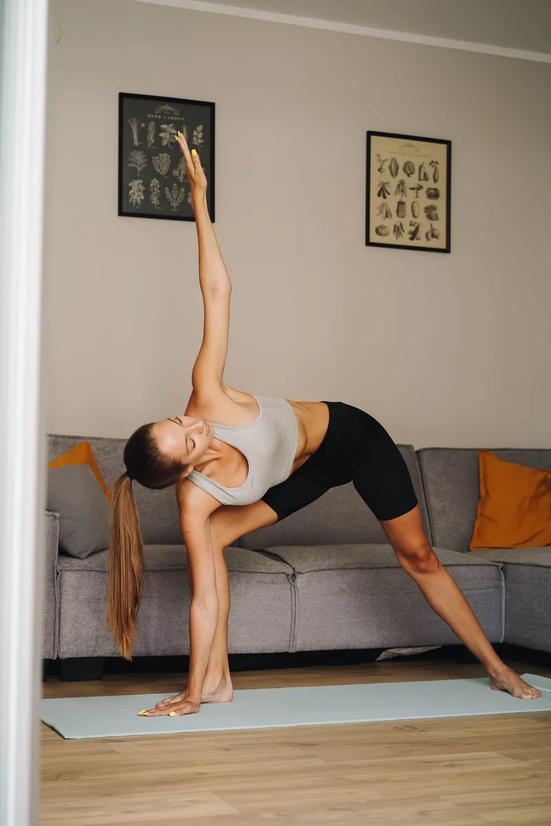 Mulher em Trikonasana na sala de casa, tronco estendido lateralmente com um braço para baixo e outro para cima