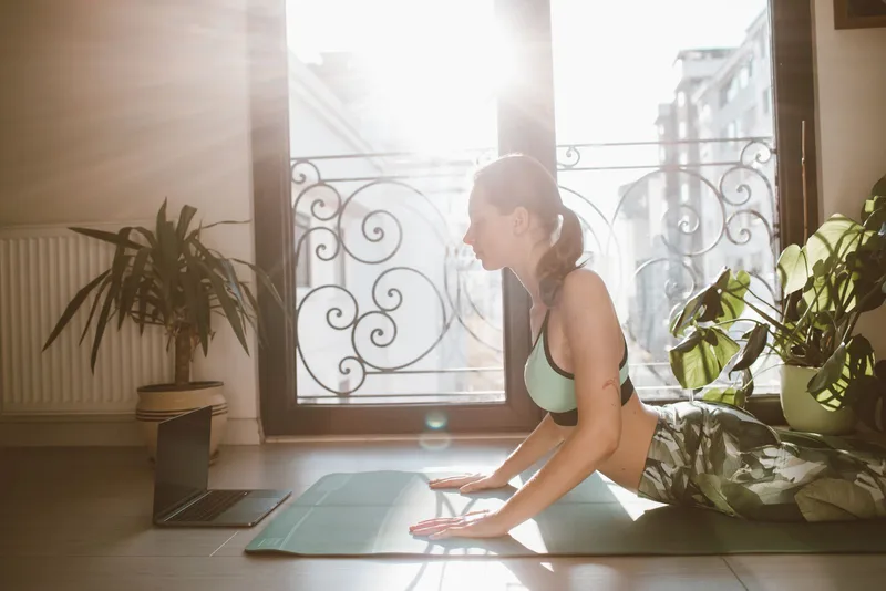 Mulher em Bhujangasana, tronco elevado com as mãos apoiadas no colchonete, em casa