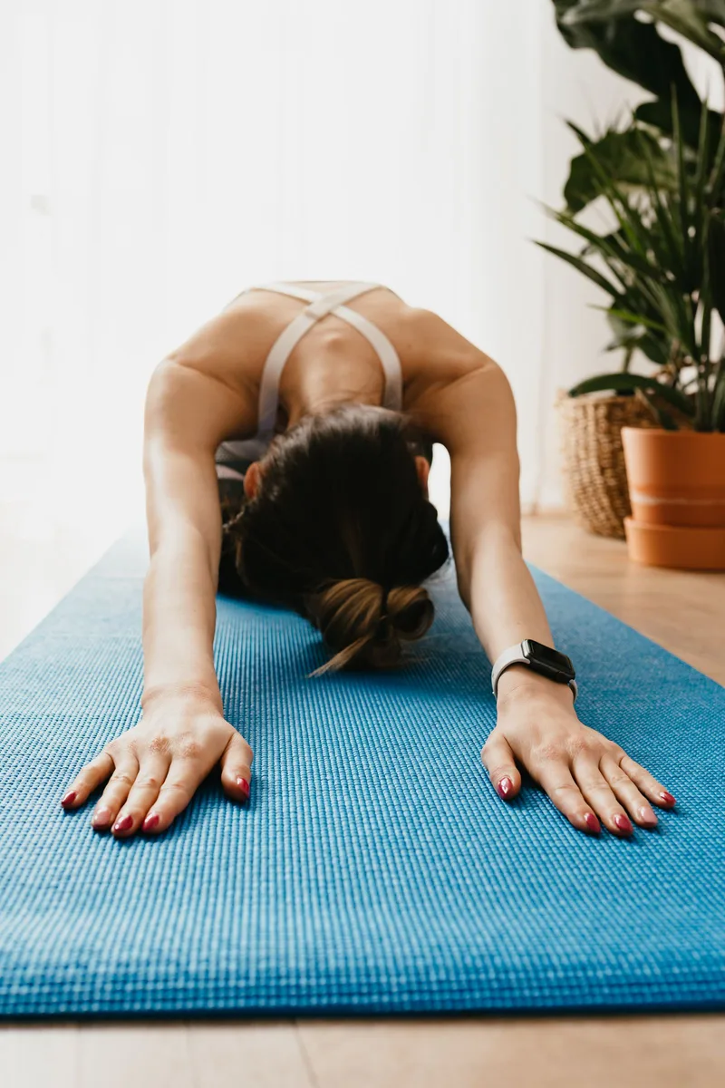 Mulher em Balasana, quadris apoiados nos calcanhares e braços estendidos à frente sobre o colchonete
