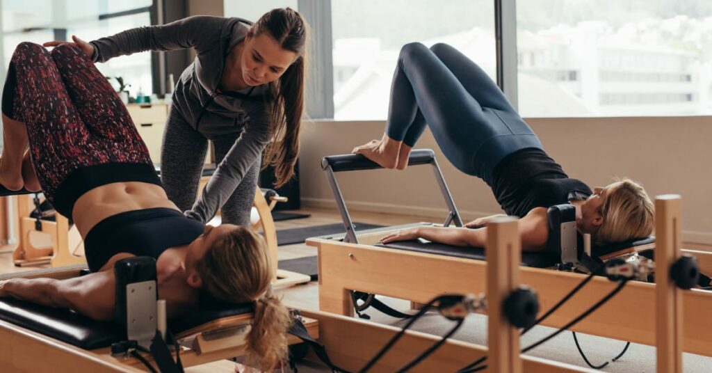 instrutora ajudando duas alunas com pilates no cadillac