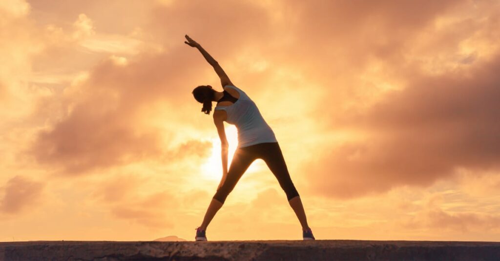 mulher fazendo alongamento no por do sol